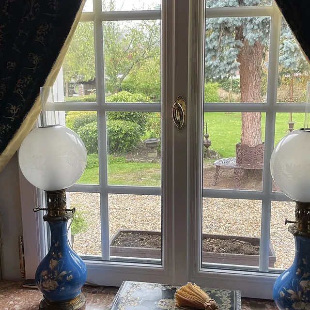 Fenêtre encadrée de rideaux avec deux lampes à pétrole bleues anciennes.
