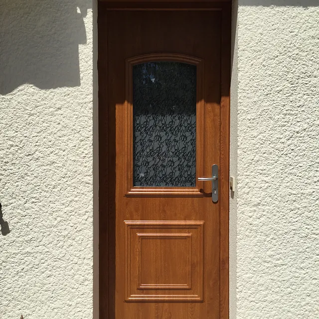 Porte d'entrée en bois marron avec vitre arquée décorative.
