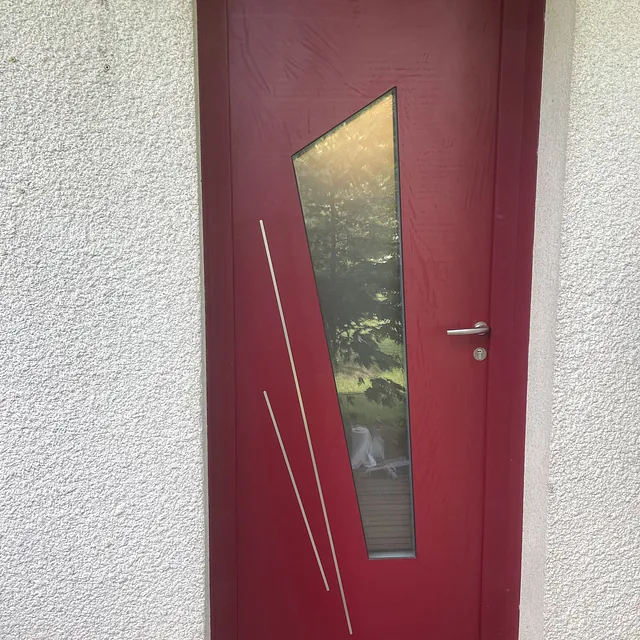Porte d'entrée rouge moderne avec vitre géométrique asymétrique.