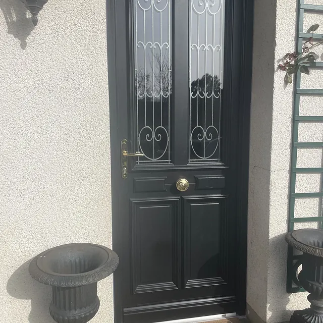 Porte d'entrée noire à double vitrage décoré et poignée dorée.